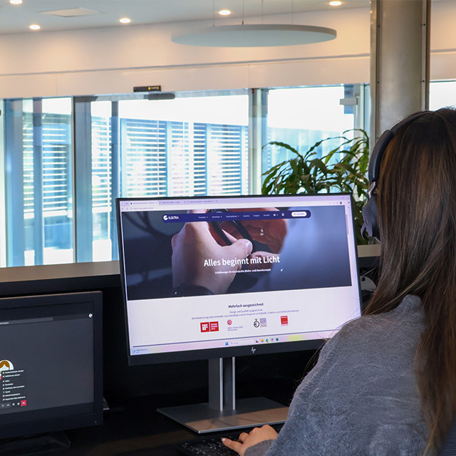 Eine Person arbeitet an einem Computer, während das Licht im Empfangsbereich eine einladende Atmosphäre schafft.