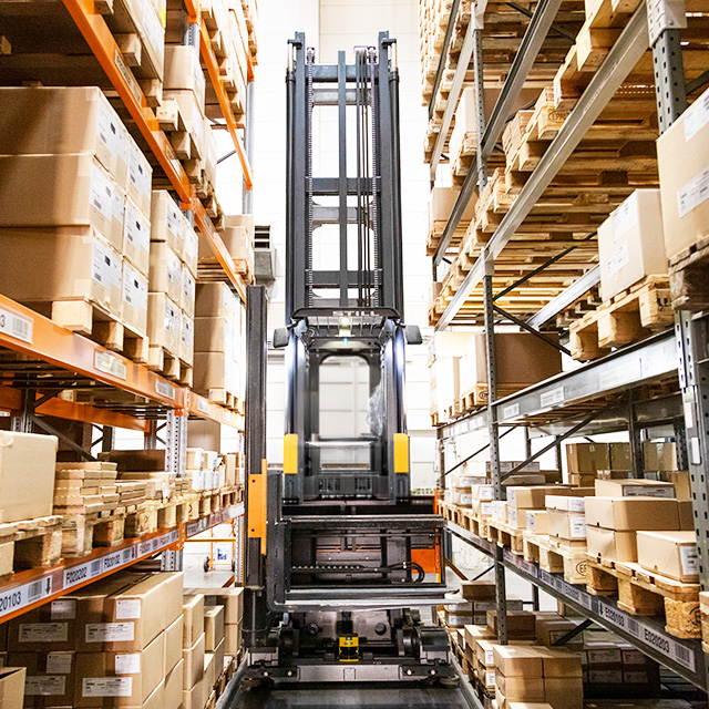 Gabelstapler zwischen hohen Regalen mit vielen Kartons in einem Lager