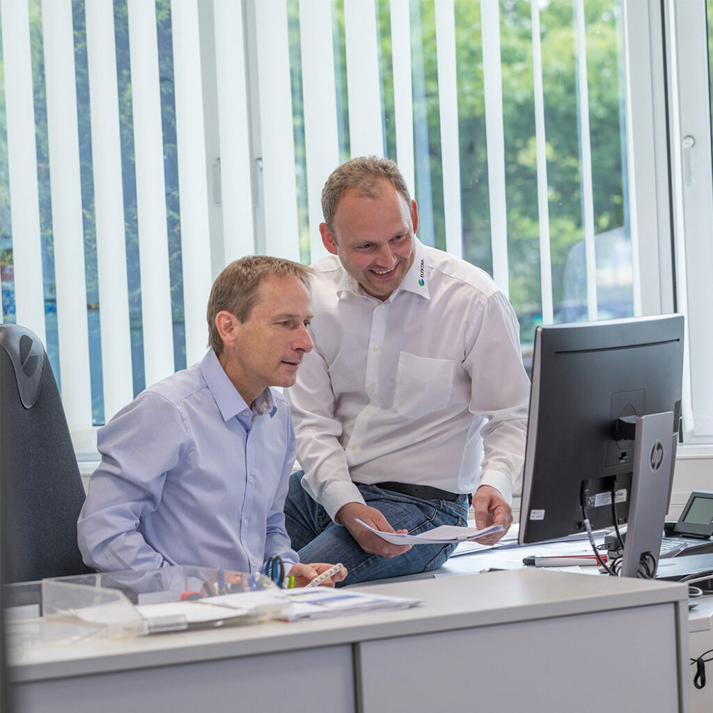 Zwei Personen arbeiten gemeinsam an einem Computer, um eine innovative Industrielösungs-Planung zu besprechen und zu entwickeln.