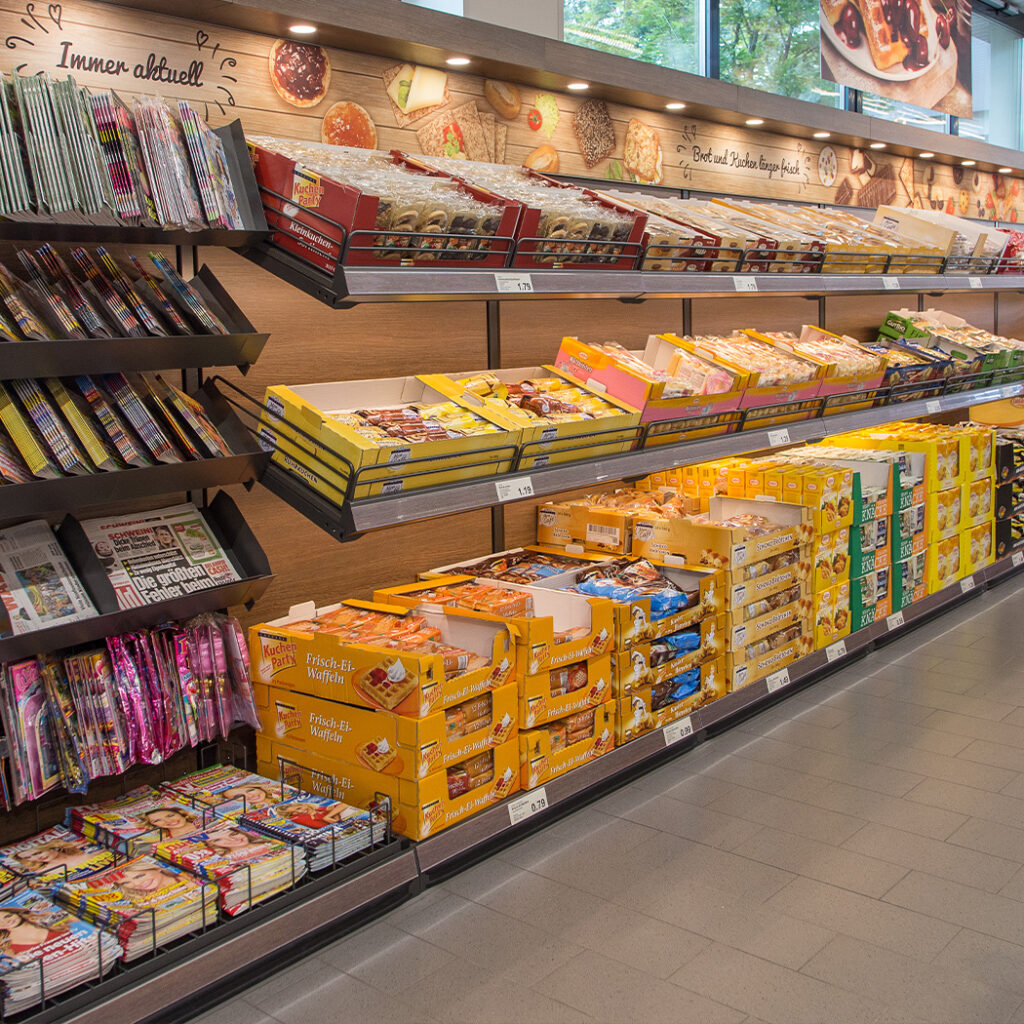 Ein modernes Ladenbau-Design zeigt ein Zeitungs- und Gebäckregal mit einer bunten Auswahl an Snacks und Zeitschriften.