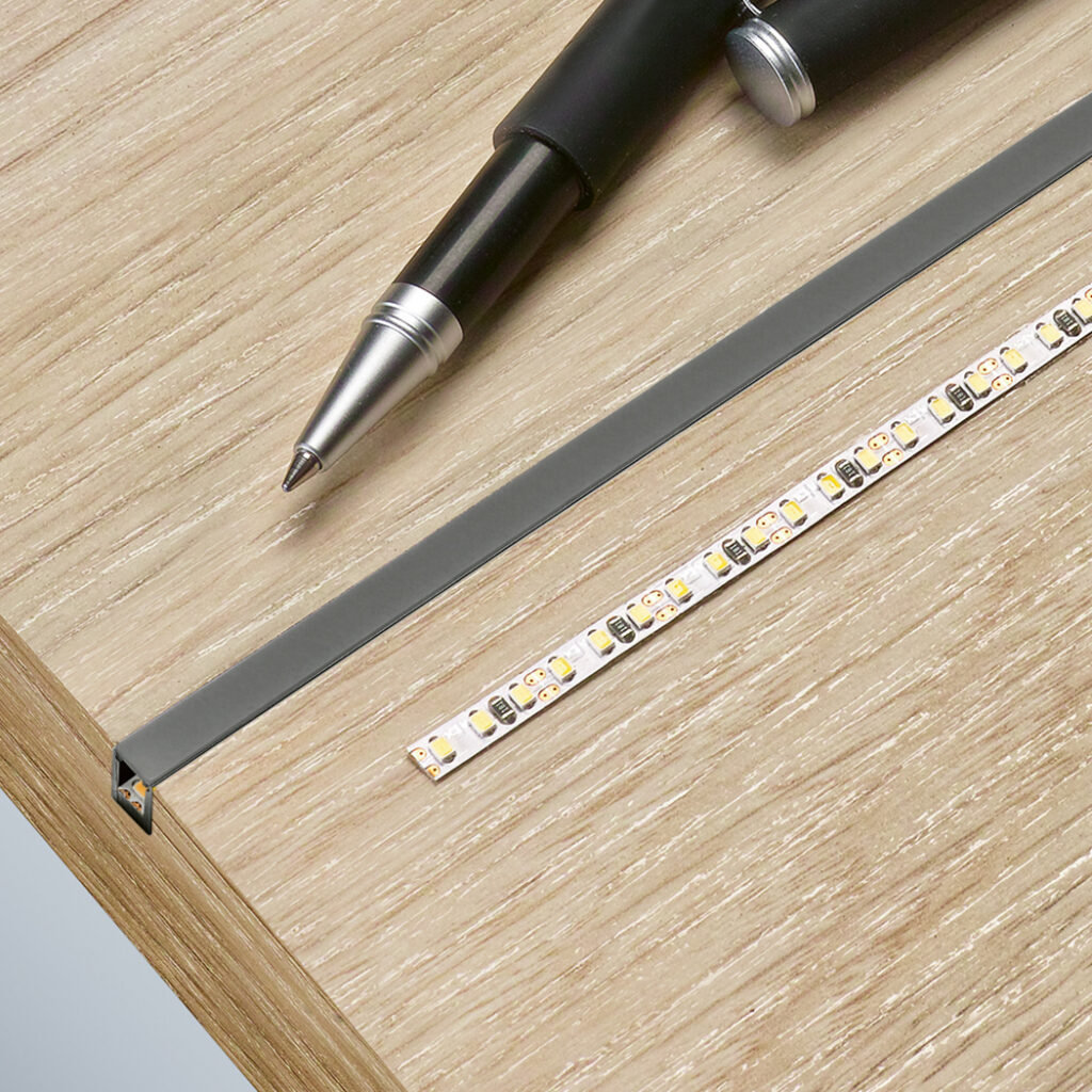 The illustration shows an installation scenario featuring LED strips and a pen for scale on a wooden surface.