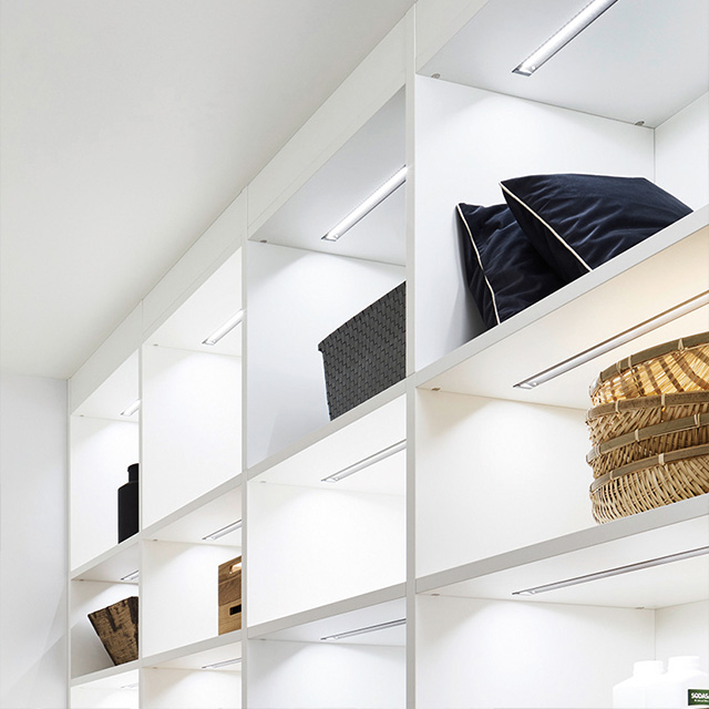 A modern white shelf with LED lighting displays stylish cushions and decorative baskets.