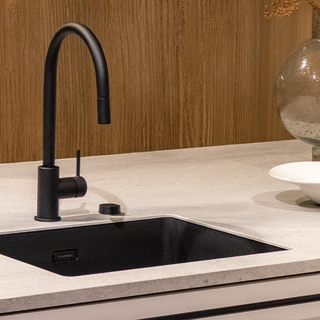 Moderne Küchenspüle mit eleganter schwarzer Armatur, umgeben von stilvollem Holz und zeitgemäßer Beleuchtung.