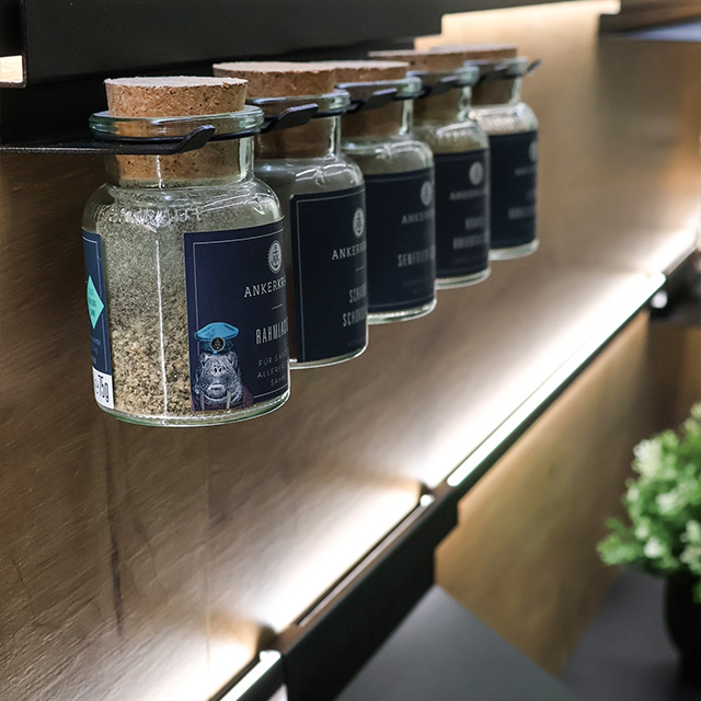 A stylish spice jar holder displays several jars of spices, illuminated by a modern lighting installation.
