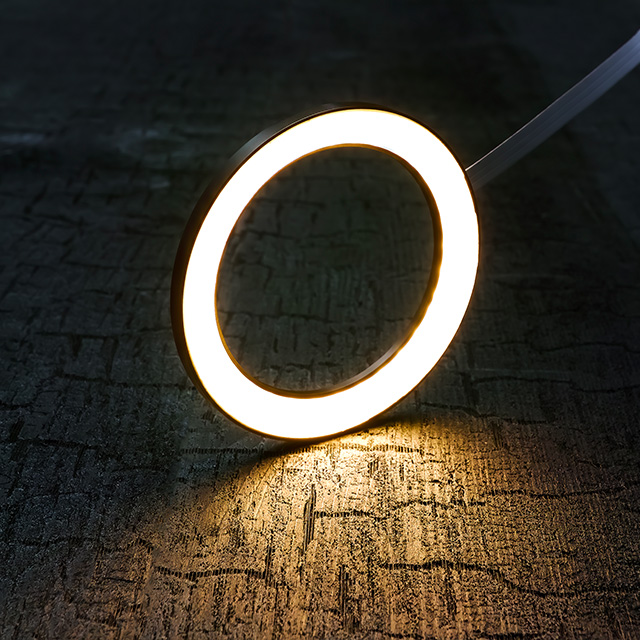 Ein runder LED-Lichtkreis strahlt warmes Licht auf eine strukturierte Holzoberfläche, was eine angenehme Atmosphäre schafft.