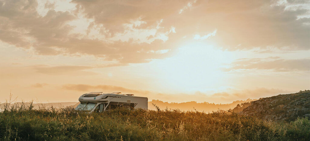 Ein modernes Micro-Wohnmobil steht in einer malerischen Landschaft bei Sonnenuntergang, umgeben von sanften Hügeln.