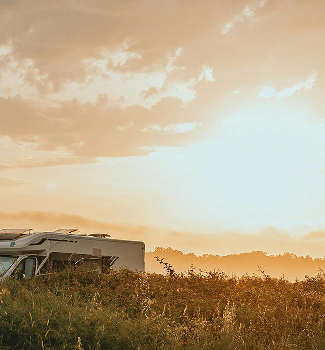 Ein modernes Micro-Wohnmobil steht in einer malerischen Landschaft bei Sonnenuntergang, umgeben von sanften Hügeln.