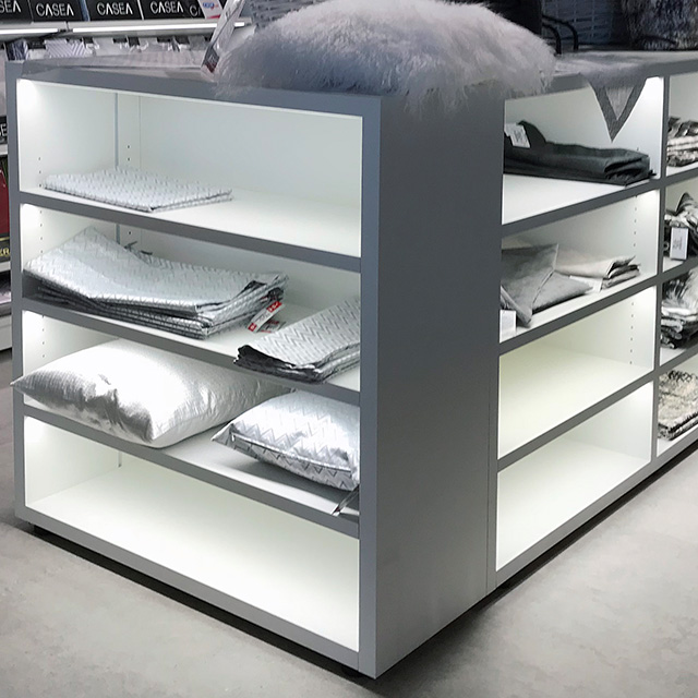 Ein modernes Verkaufsregal mit beleuchteten Fächern präsentiert dekorative Kissen und Textilien in einem stilvollen Laden.