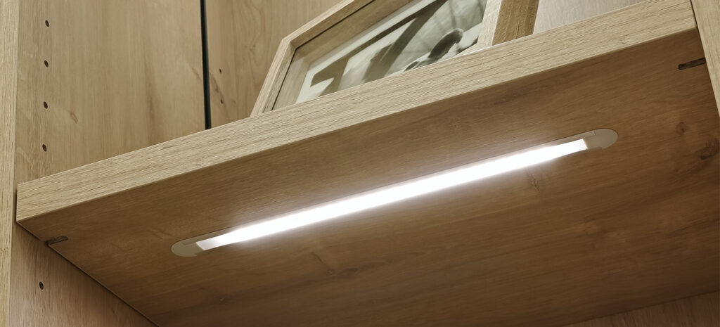 Ein modernes Vario-Regal mit integrierter LED-Beleuchtung, das eine warme Atmosphäre im Raum schafft.