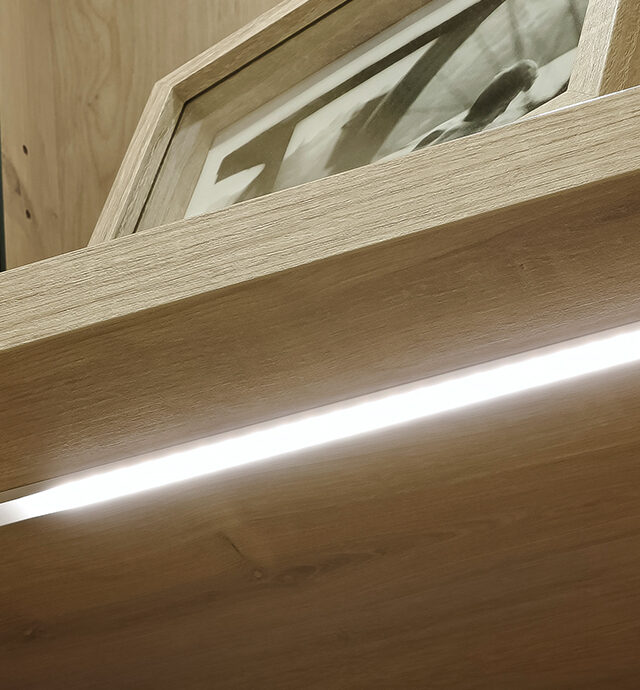 Ein modernes Vario-Regal mit integrierter LED-Beleuchtung, das eine warme Atmosphäre im Raum schafft.