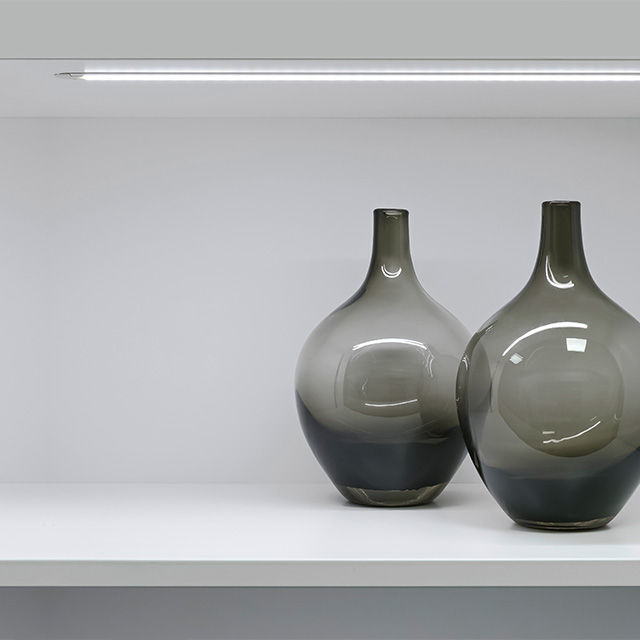 The illuminated Vario D10 shelf displays stylish vases in elegant shades of gray, which harmoniously accent the room.