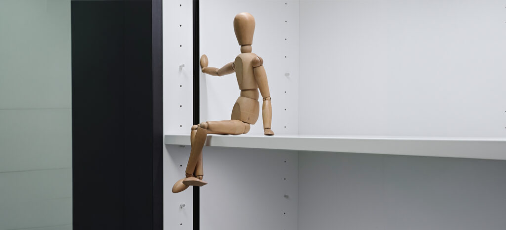 Eine Holz-Gleiderpuppe sitzt lässig auf einem weißen Regal, das einen modernen Raumakzent setzt.